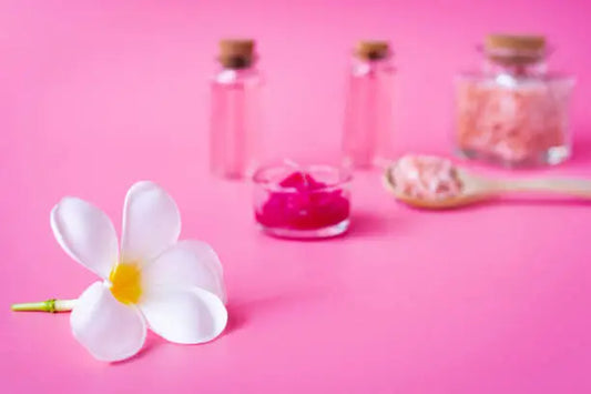 Frascos de aceites esenciales y flores sobre una superficie rosa, representando el uso de aromaterapia para mejorar la experiencia sexual y el bienestar.