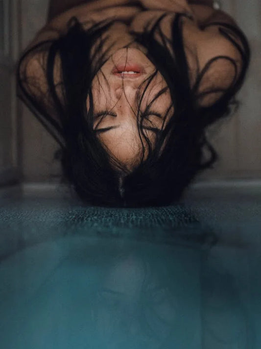 Retrato artístico de una mujer con el cabello suelto cayendo hacia adelante, reflejada parcialmente en una superficie de agua, capturando una atmósfera de tranquilidad, misterio y satisfaccion