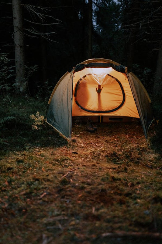 Tienda de campaña iluminada en un bosque oscuro, simbolizando la intimidad y la apertura en la comunicación sexual dentro de una relación de pareja.