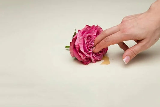 Mano acariciando delicadamente una rosa rosa sobre una superficie, representando el autoconocimiento y la exploración íntima con suavidad y cuidado. La imagen evoca sensualidad, autoaceptación y conexión con el cuerpo